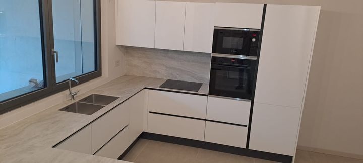 Cucina bianca lucida ad angolo con top nero e colonna forno/microonde a scomparsa.